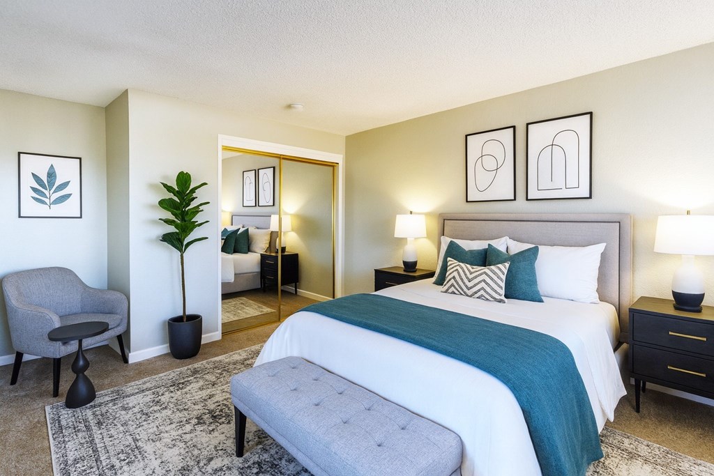 A bedroom with a large bed and a grey chair.