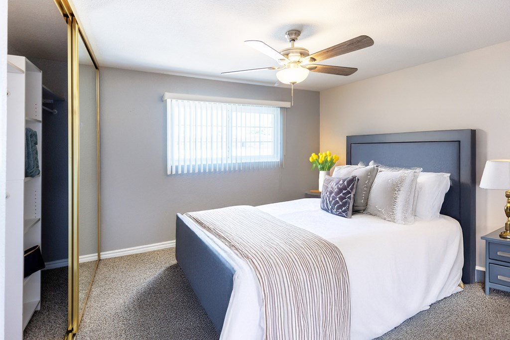 A bedroom with a bed, a ceiling fan, and a window with blinds.