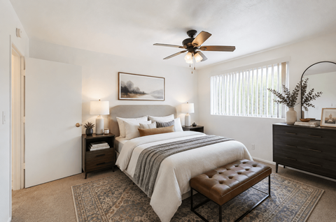 A bedroom with a bed, a bench, and a ceiling fan.