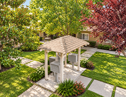 A gazebo is surrounded by a garden with a house in the background.