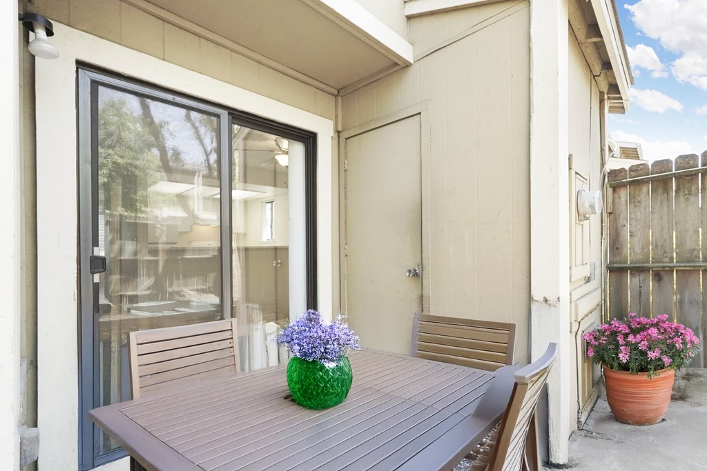 A table with a vase of flowers on it sits on a patio.