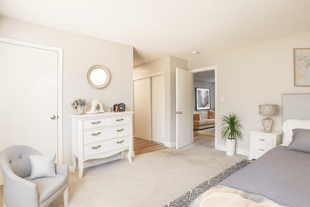 A white bedroom with a grey bed and a white chair.