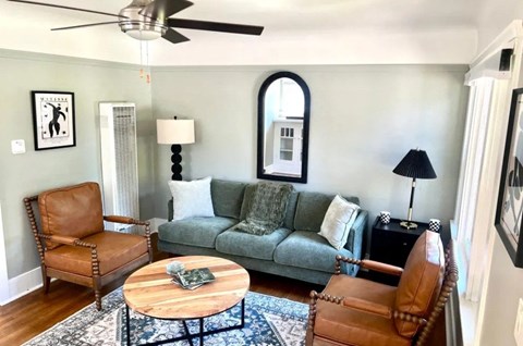 A living room with a grey couch, a brown leather chair, a wooden coffee table and a painting on the wall.