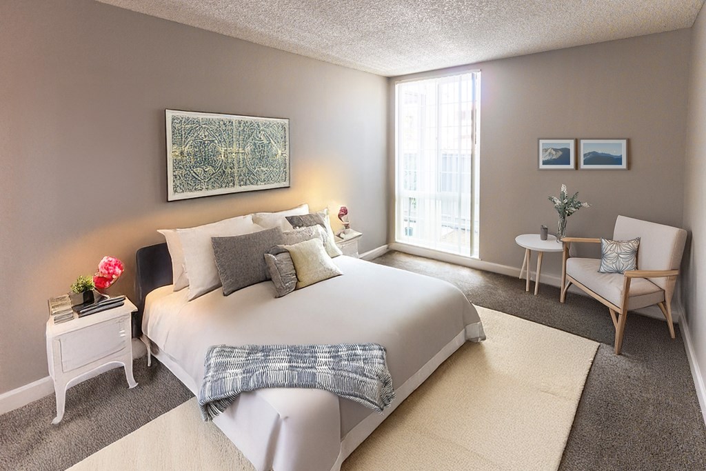 A bedroom with a large bed, a chair, and a painting on the wall.