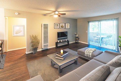 A living room with a grey couch, a coffee table, a television, and a balcony with a chair and a table.