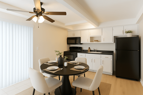 A black refrigerator sits in a kitchen with white cabinets and a table set for two.