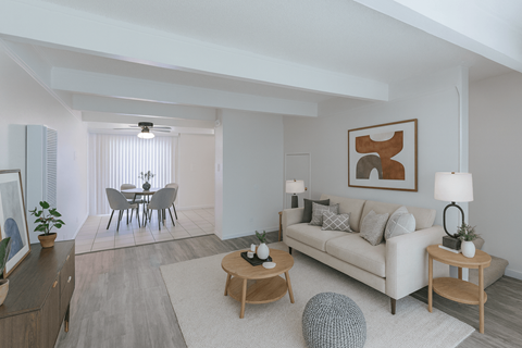 A living room with a white couch, a dining table with chairs, and a ceiling fan.