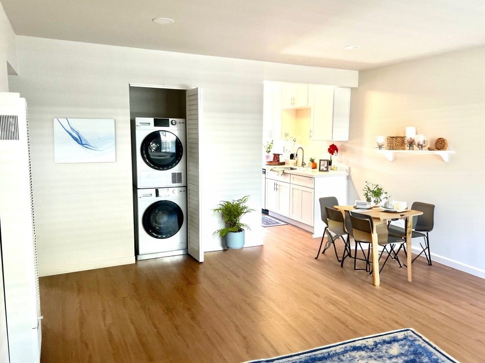 a living room with a washing machine and a kitchen with a table and chairs
