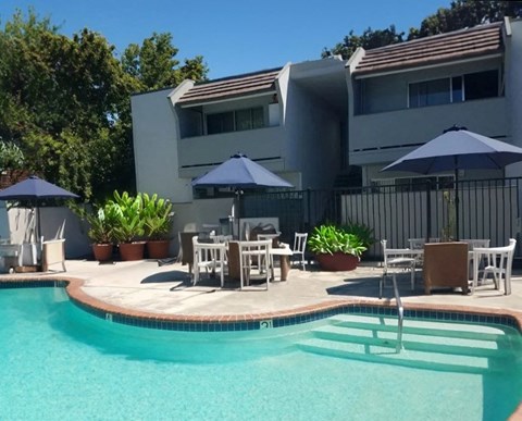 a swimming pool with tables and umbrellas in front of a house