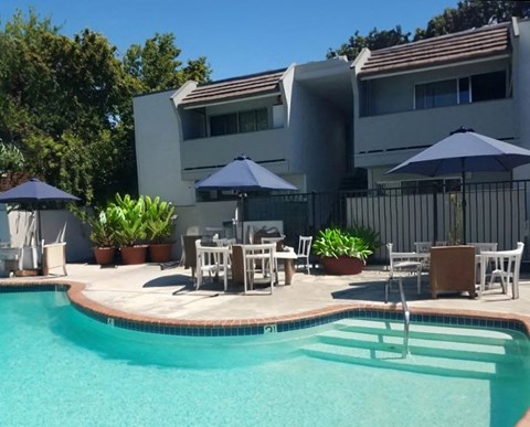 a swimming pool with tables and umbrellas in front of a house