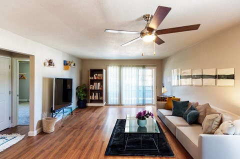 A living room with a white couch, a glass coffee table, and a ceiling fan.