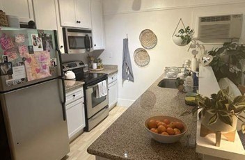 A kitchen with a refrigerator, oven, microwave, and a bowl of fruit on the counter.