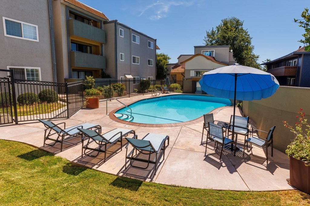 A pool surrounded by chairs and an umbrella in a backyard.