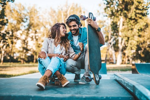 A man and a woman are sitting on a skateboard ramp, with the man holding the woman's hand.