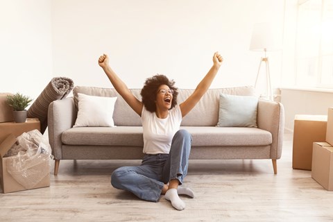 A woman is sitting on the floor with her arms raised in excitement.