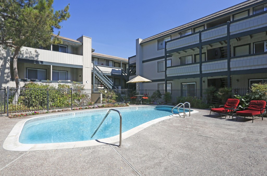 A swimming pool with red chairs and a white umbrella.