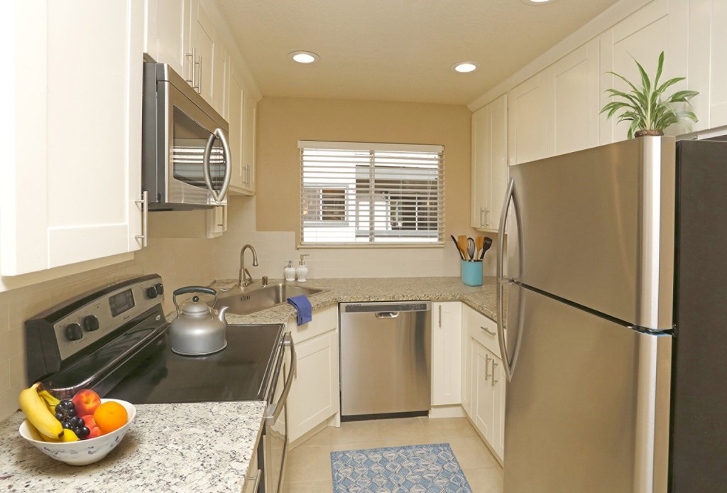 A kitchen with a stove, refrigerator, and a bowl of fruit on the counter.