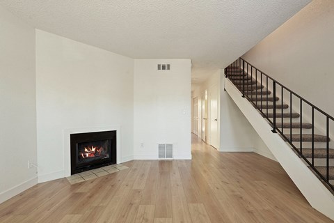 A spacious living room with a fireplace and a staircase.