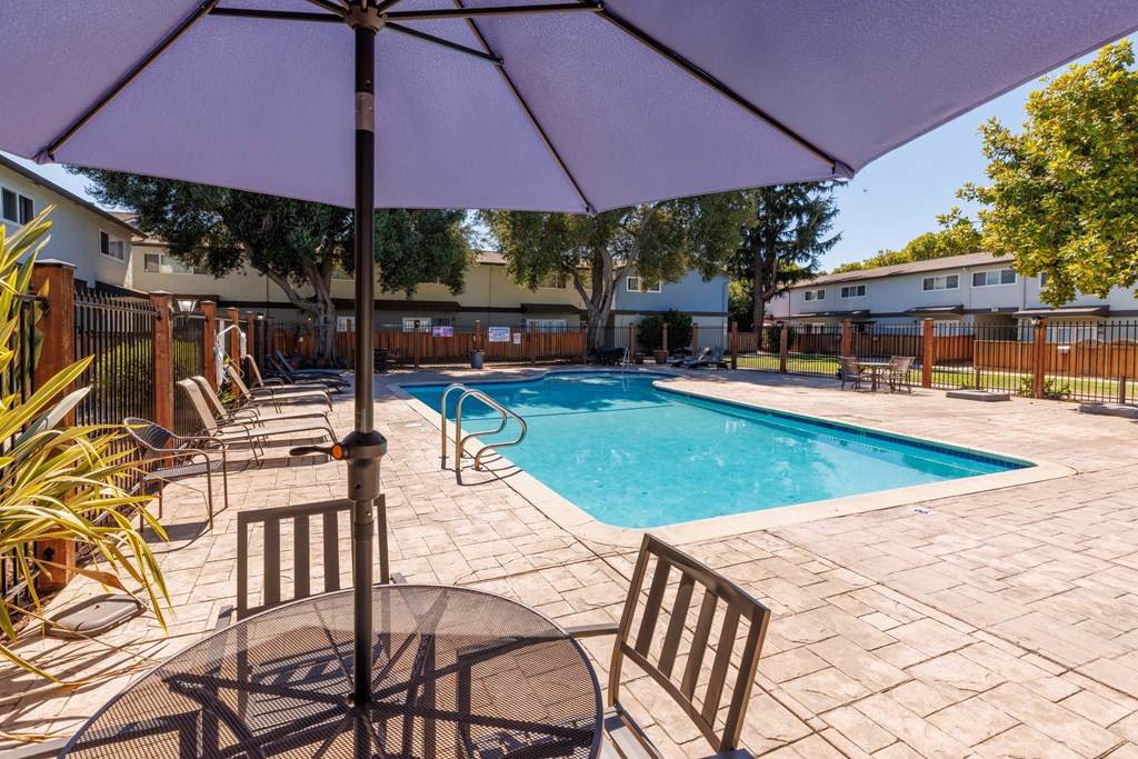 A purple umbrella is over a table in a backyard with a pool.