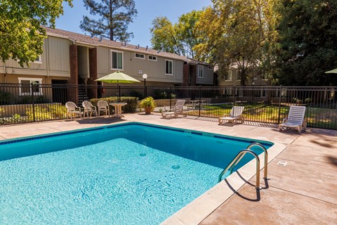 A swimming pool in a backyard with a fence and chairs.