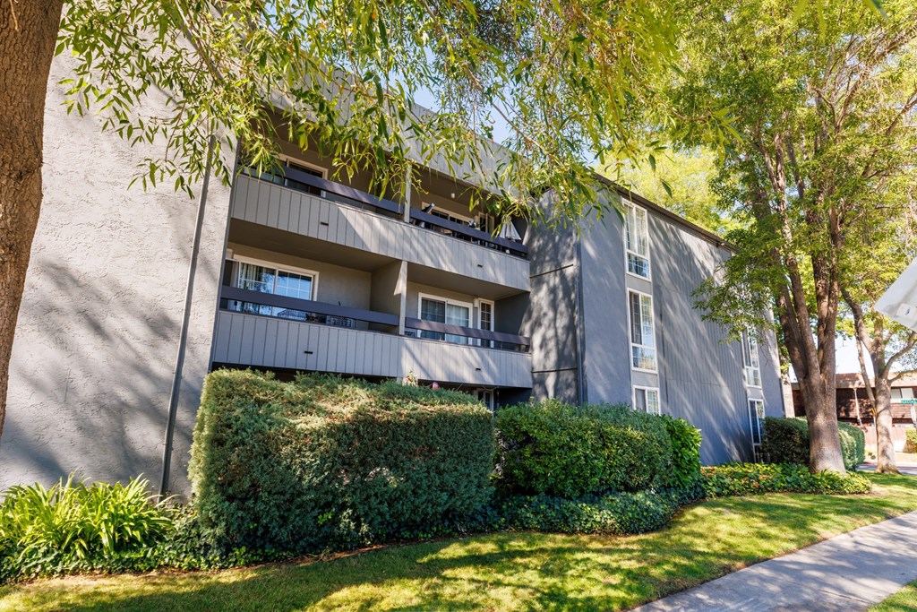 A grey apartment building with green bushes in front.