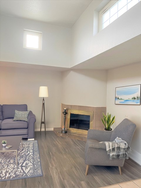 A living room with a grey couch, a grey armchair, a fireplace, and a painting on the wall.