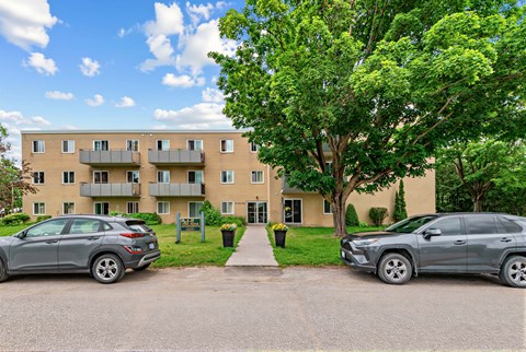 Two cars are parked in front of a building with a tree in the foreground.