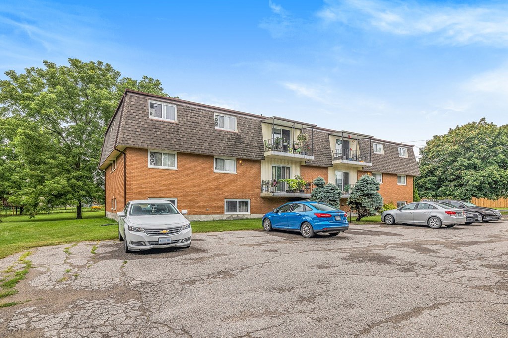A white car is parked in front of a brick building with a blue car parked in front of it.