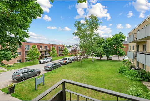 A view of a green lawn from a balcony with apartment buildings in the background.
