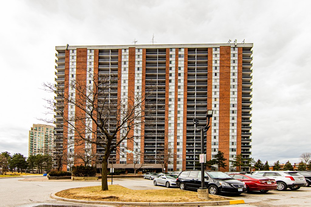 A tall apartment building with a parking lot in front.