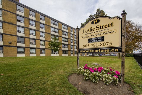 A sign for Leslie Street Apartments stands in front of a brick building.