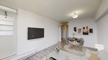 A living room with a television, a dining table and chairs, and pictures on the wall.