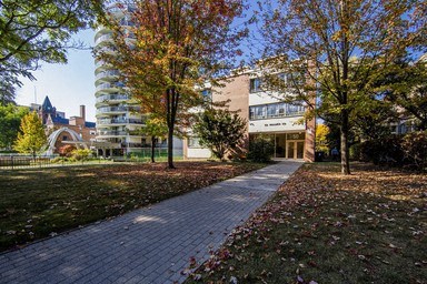 A brick walkway leads to a building with a clock tower in the background.