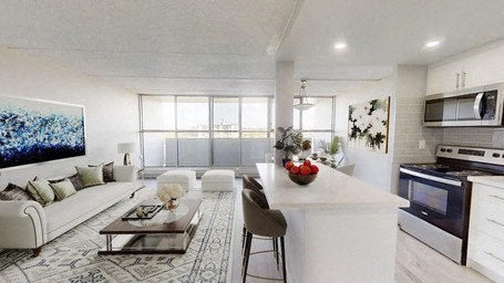 A modern kitchen with a white color scheme and a dining area with a white couch and a coffee table.