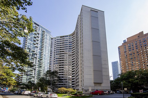 A tall building with a grey facade stands in front of a parking lot.