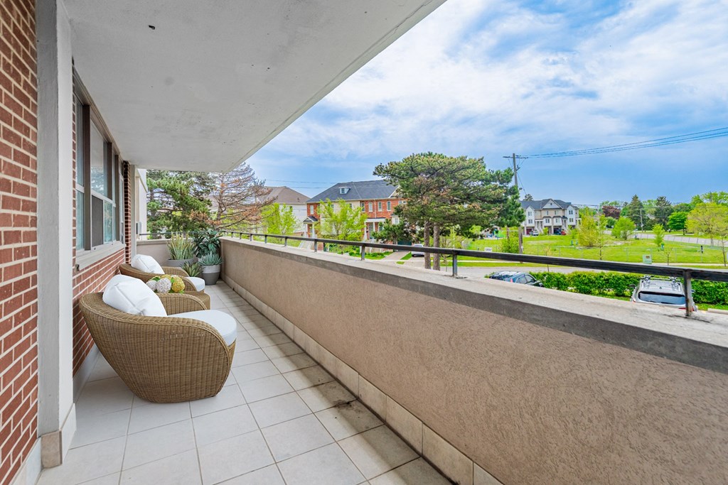 A balcony with a wicker chair and a white pillow is overlooking a residential area.