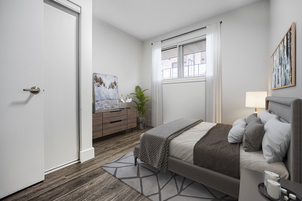 A bedroom with a bed, nightstand, and a window with a view of a balcony.