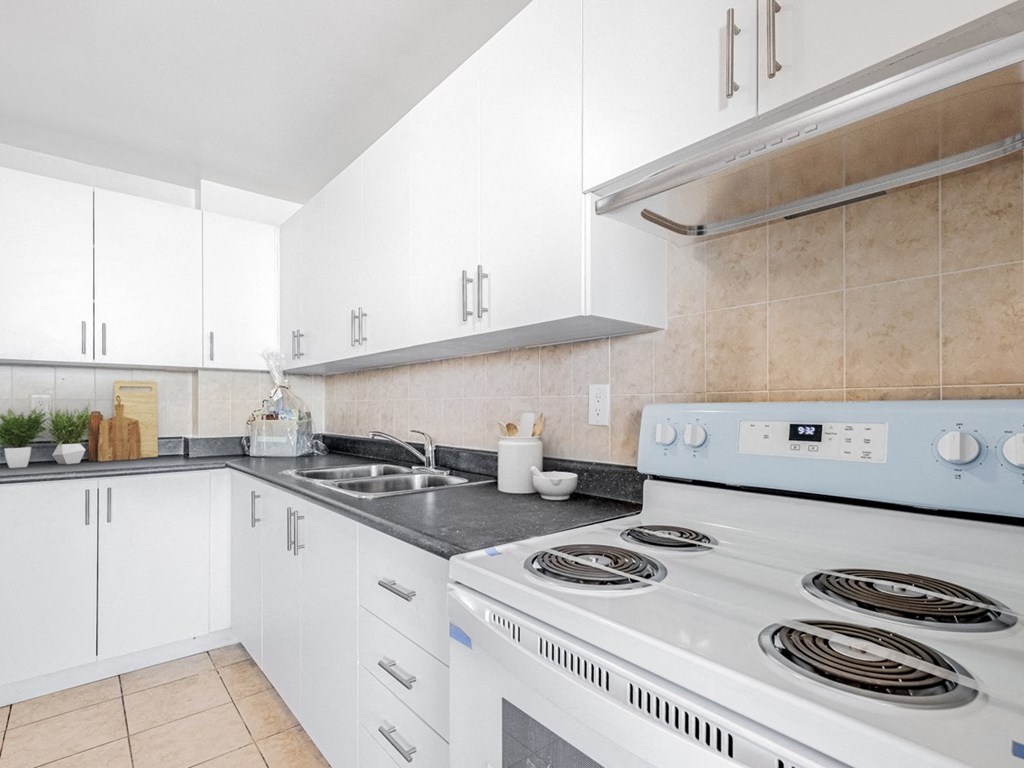 A white stove with four burners is in a kitchen with white cabinets.