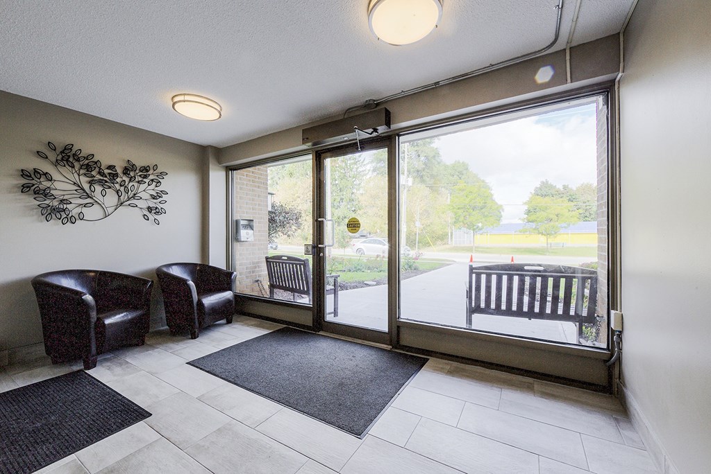 A room with a wall art, two chairs, a bench and a door leading outside.