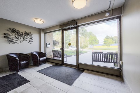 A room with a wall art, two chairs, a bench and a door leading outside.