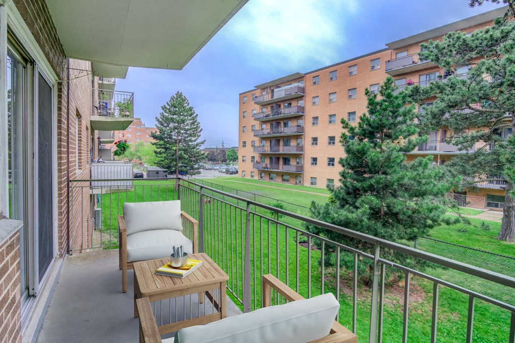 A balcony with a table and chairs overlooks a grassy area and apartment buildings.