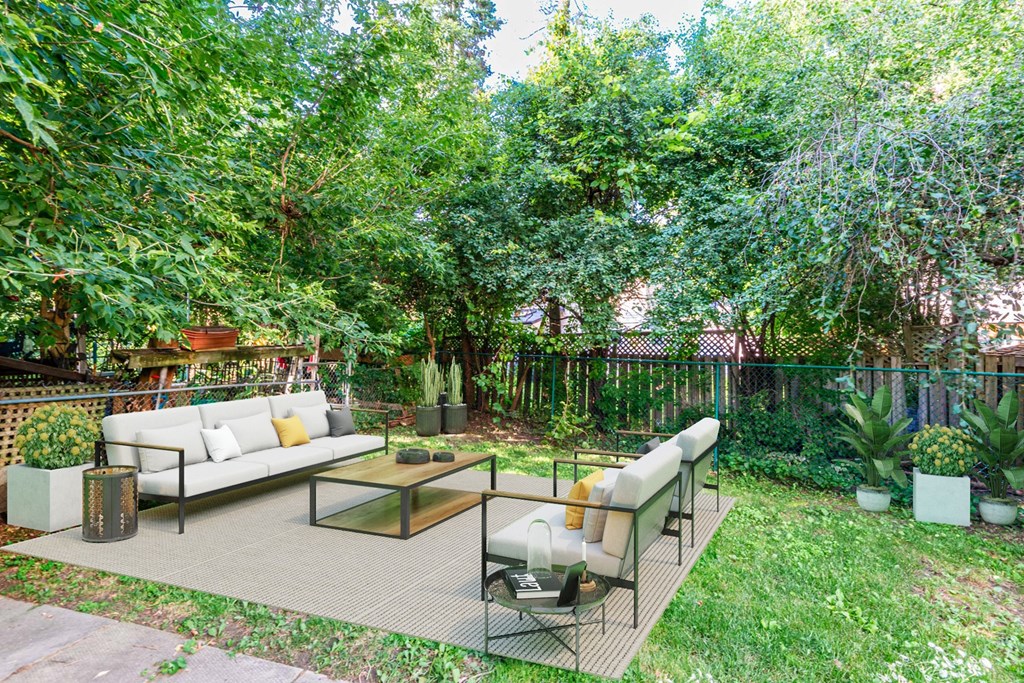 A backyard with a white couch and a glass coffee table.