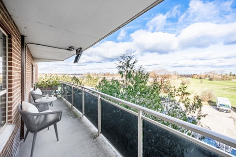 A balcony with a table and chairs overlooking a field.