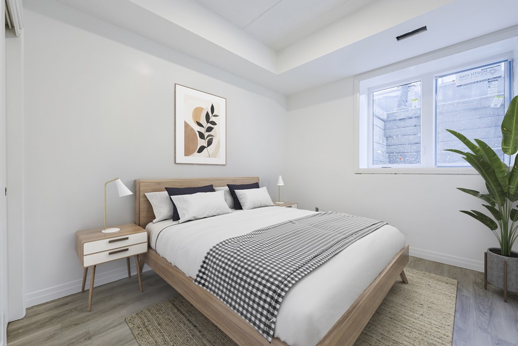 A bedroom with a bed, nightstand, and a plant.