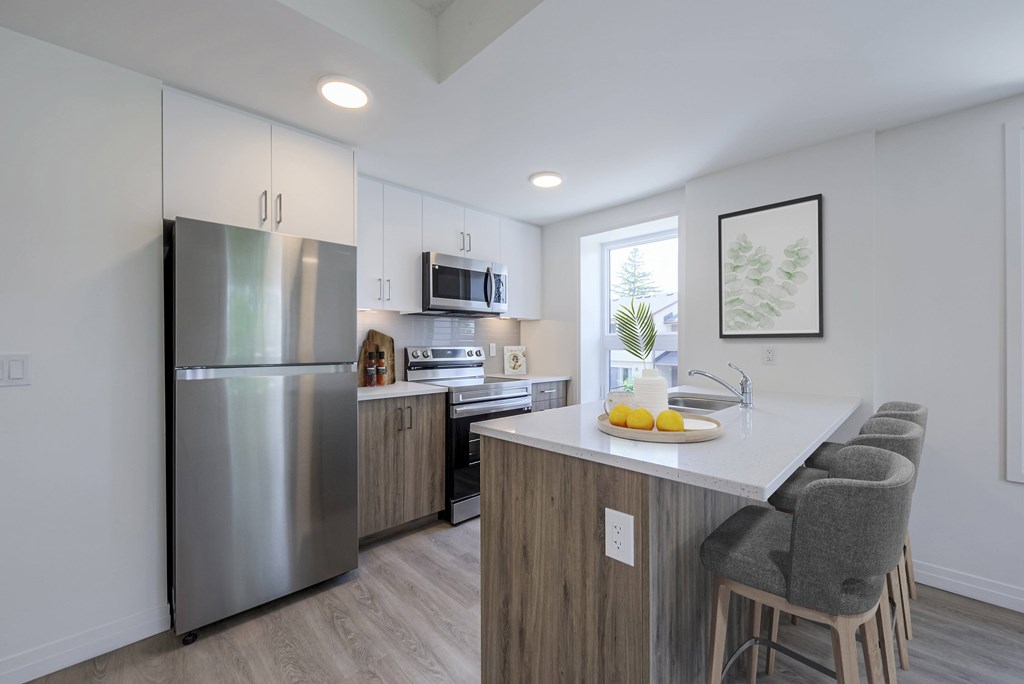 A kitchen with a stainless steel refrigerator, wooden countertops, and grey barstools.