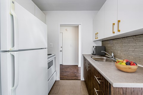 A kitchen with a white fridge, wooden cabinets and a bowl of fruit on the counter.