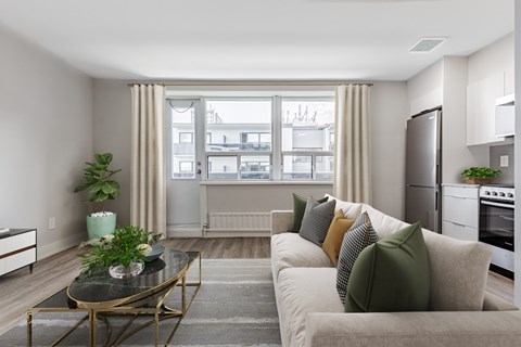 A modern living room with a glass table and a couch with green pillows.