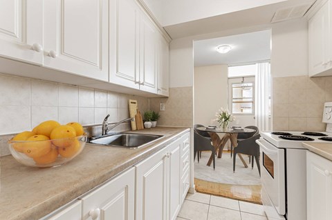 A kitchen with white cabinets and a bowl of oranges on the counter.