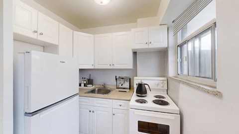 A white kitchen with a stove, sink, and cabinets.