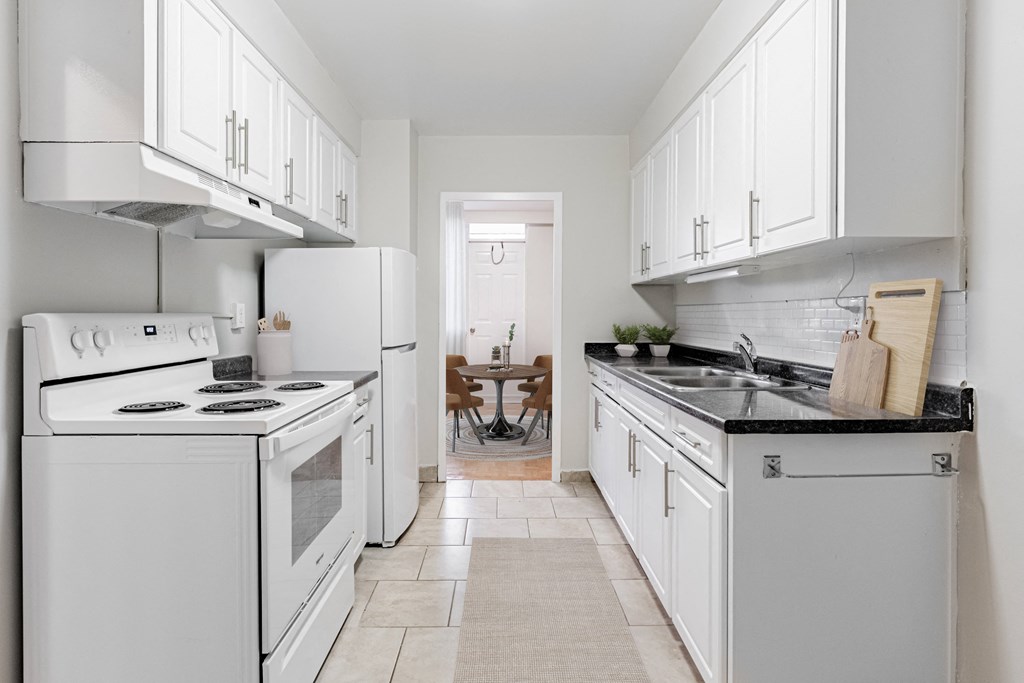 A white kitchen with a black counter top and a tile floor.